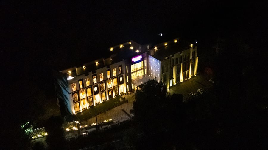 An aerial view of a building at night reveals its illuminated structure and surrounding area, emphasising its bright presence in the dark | Sukama Resort & Spa, Nainital