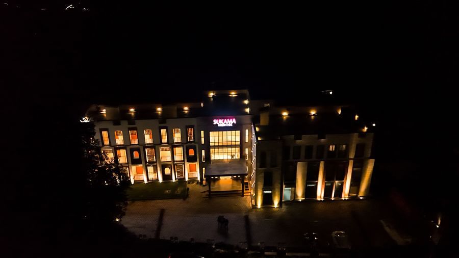 A large building is illuminated at night, with lights highlighting its architectural features and creating a warm glow | Sukama Resort & Spa, Nainital