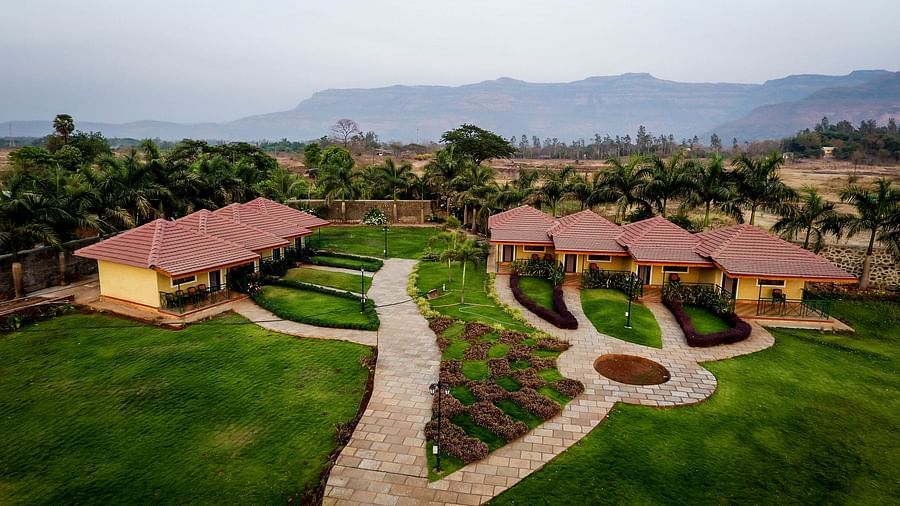 Aerial view of a stone pathway winds through a lush green lawn, leading to a row of Deluxe Cottages at The Kanila Resort