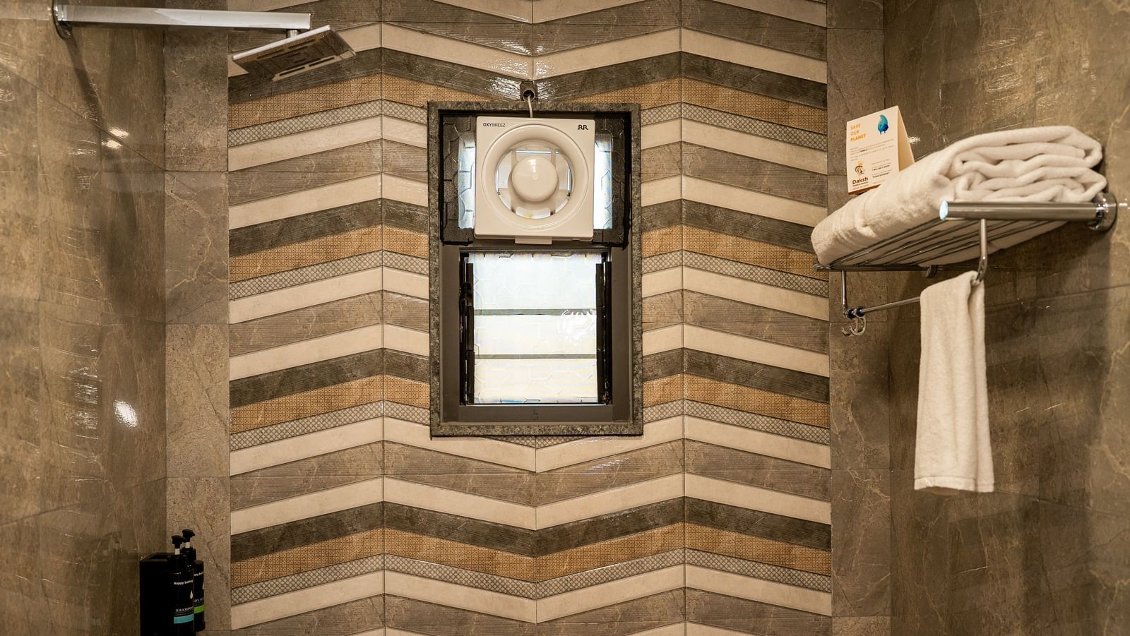 A modern bathroom at Daksh The Grand Gowardhan, Dwarka, featuring stylish chevron-patterned tiles and a shower area.