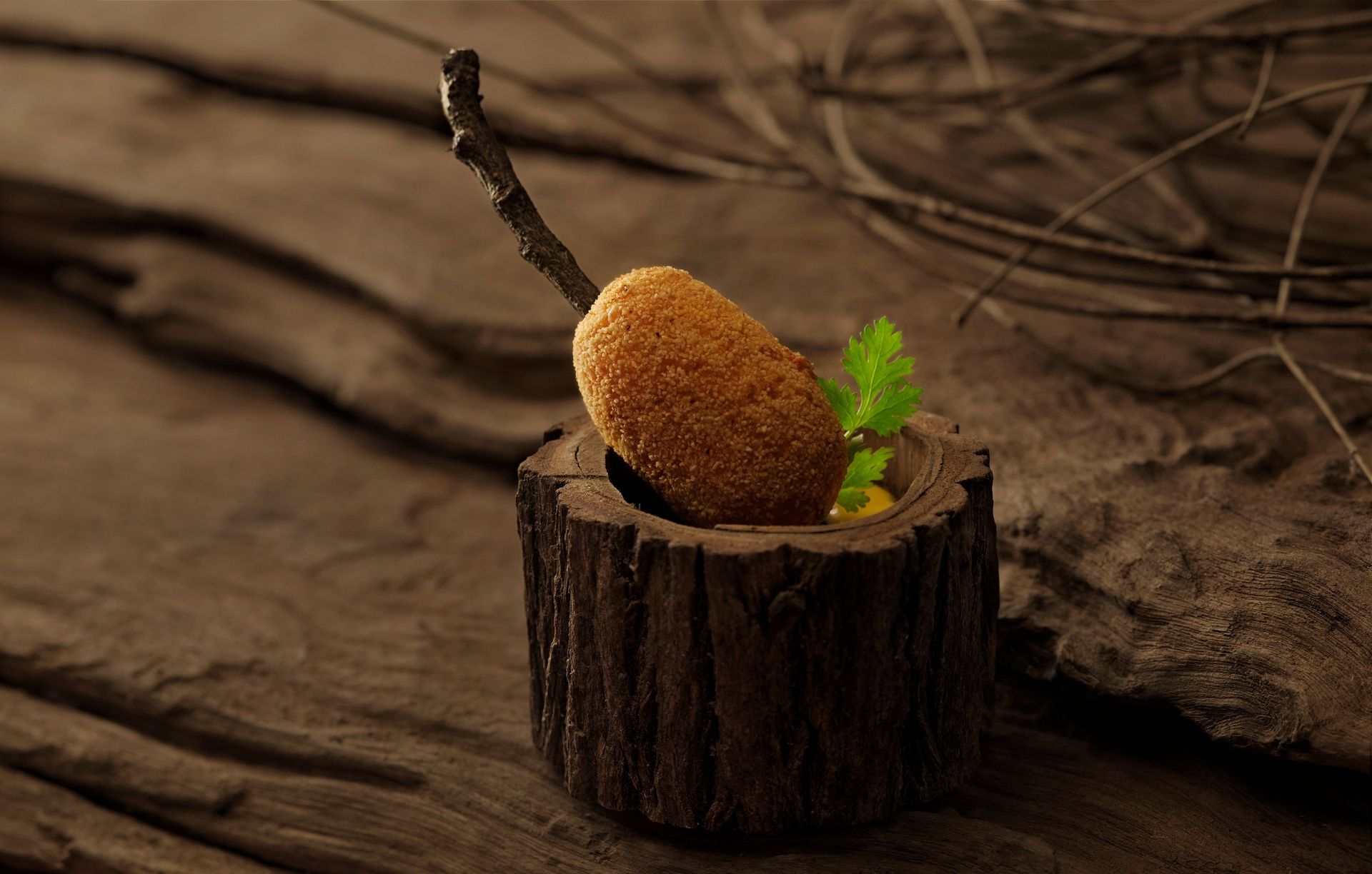 Crispy croquette in a wooden holder with a twig.