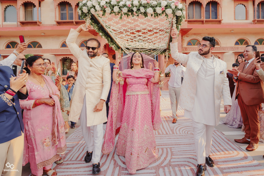Bride Ritika walking under floral canopy with family at Umaid Palace wedding