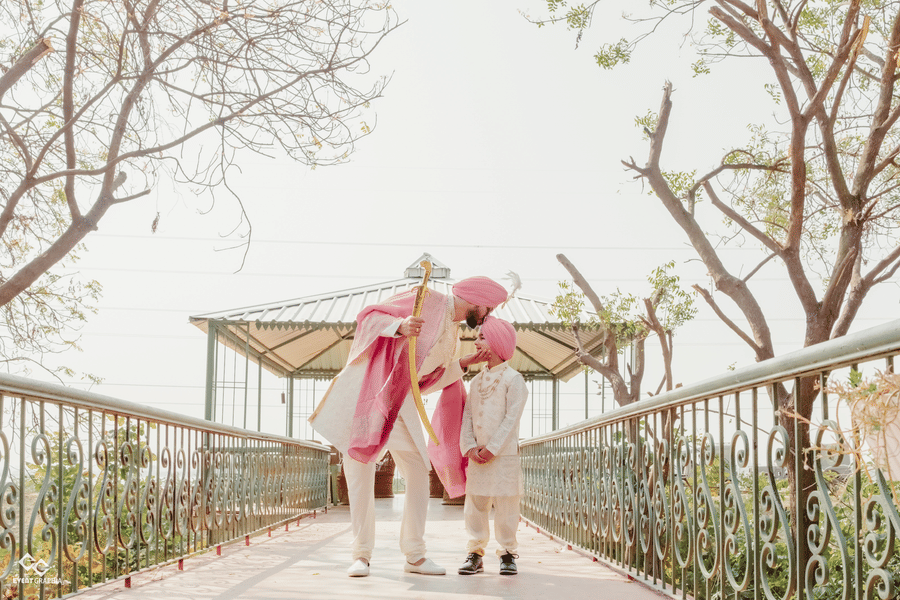 A groom and a young boy walk across an outdoor bridge surrounded by trees at Umaid Palace.
