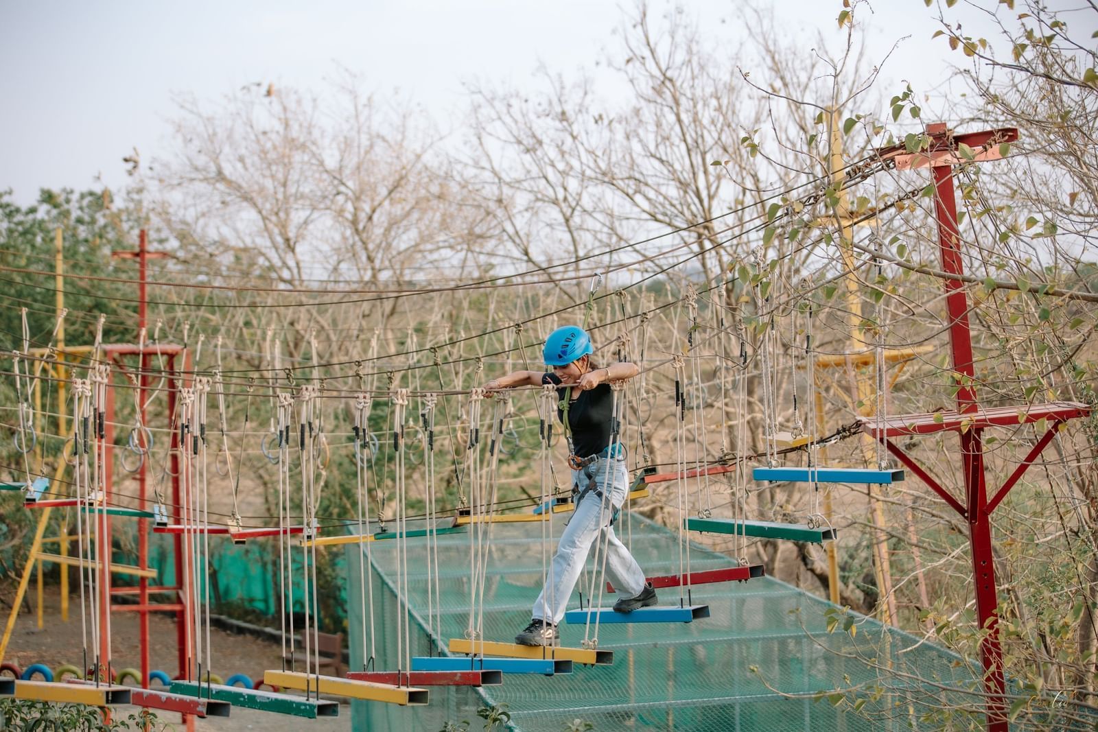 A person walks carefully across a wide, suspended log bridge on the high ropes course, at Daksh Resort & Amusement Park, Sasan Gir.