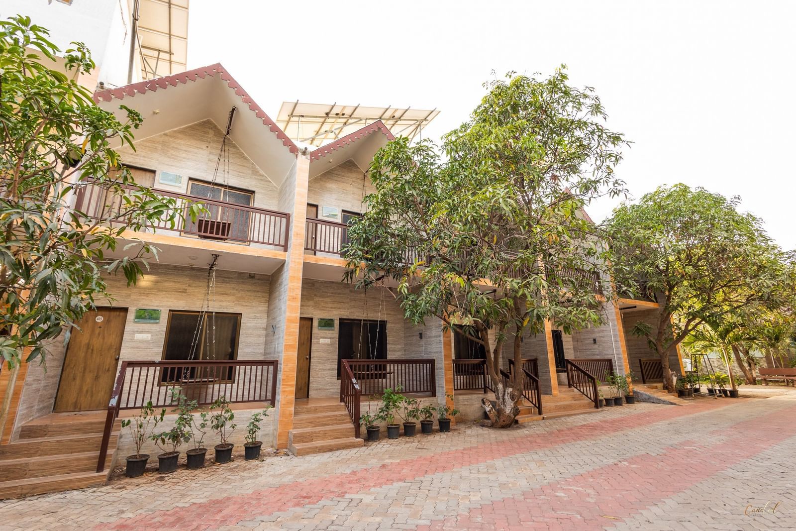Exterior view of Daksh Resort & Amusement Part featuring a two-storey resort building with balconies, trees, and a paved driveway in the front.