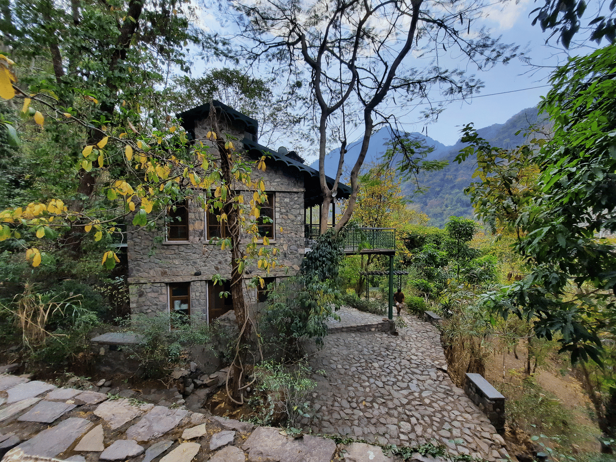 Facade view of Neemrana's Glasshouse on The Ganges amidst the nature with mountains and clear blue sky in the background.