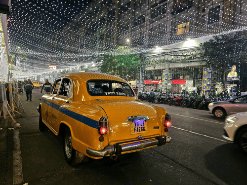A Kolkata local yellow taxi driving through the  street decorations of park street at night.
