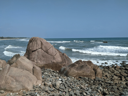 Waves crash against weathered rocks beside Mahabalipuram Beach, where the rugged coastline meets the Bay of Bengal dramatically at dusk