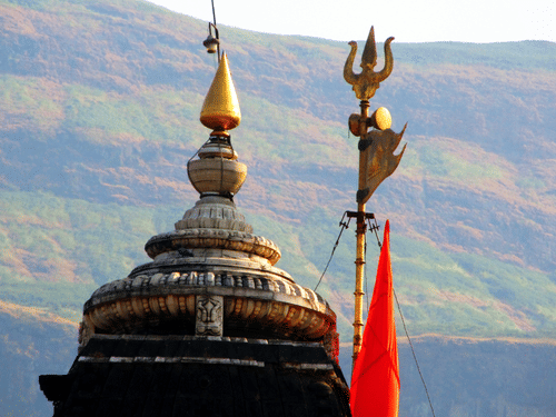 A temple dome with a golden finial and a trident symbol with hills visible in the background.