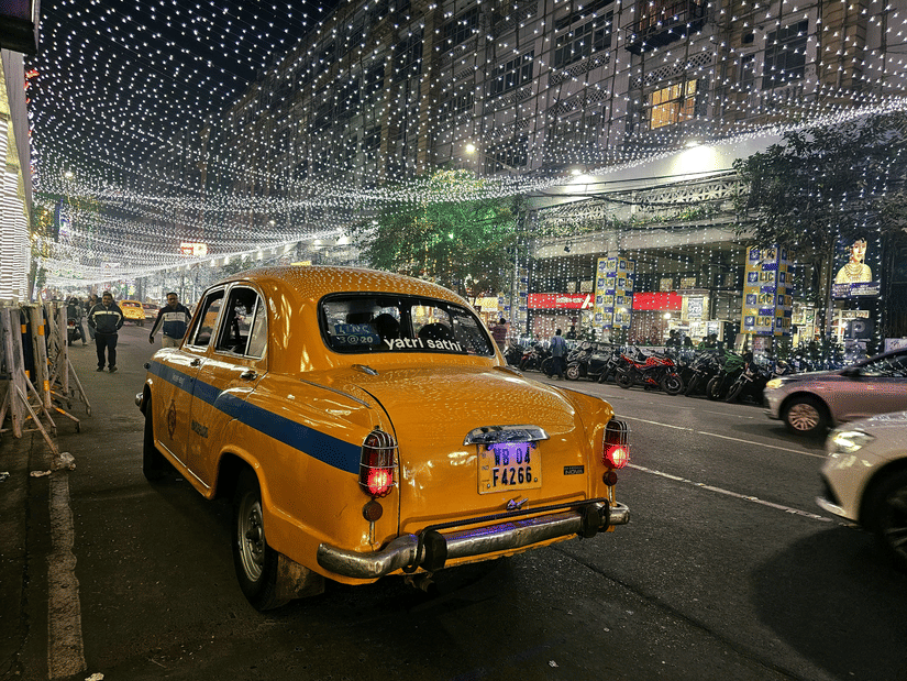 A Kolkata local yellow taxi driving through the  street decorations of park street at night.