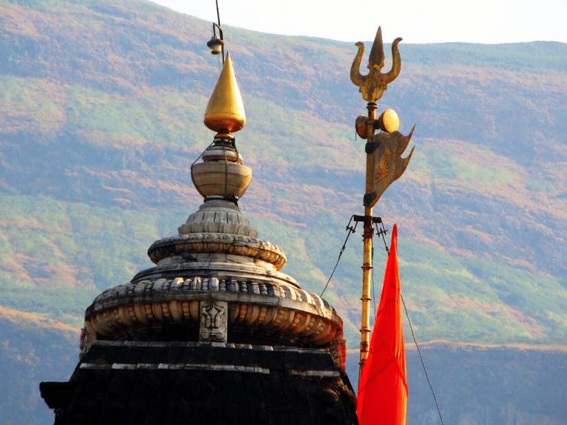 A temple dome with a golden finial and a trident symbol with hills visible in the background.
