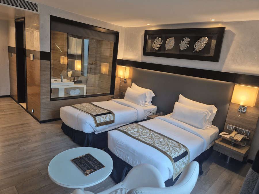 Modern hotel room featuring twin beds with decorative runners, warm lighting, and a view into the bathroom.