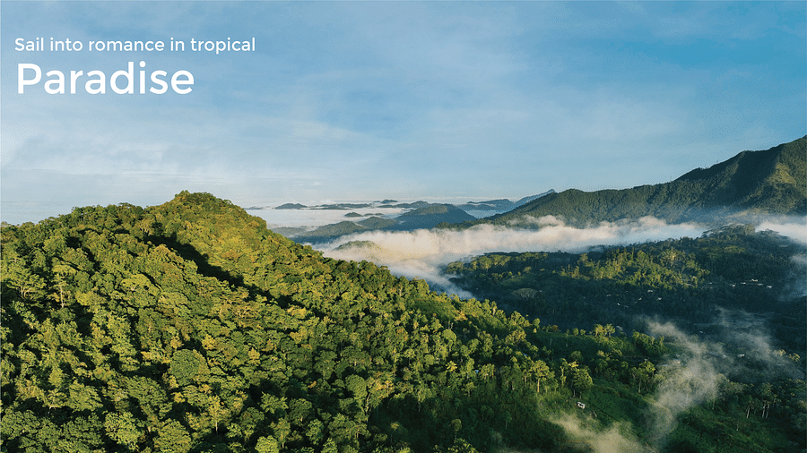Mountains covered with lush greenery as the clouds are touching their heads and the text on the banner says 'Sail into romance in tropical paradise'