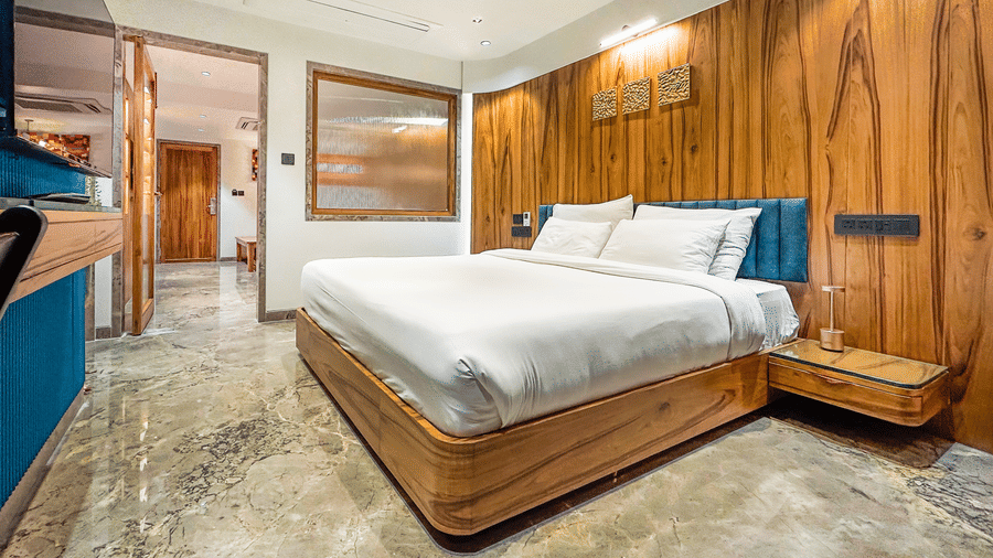 A modern bedroom with a wooden bed frame, white bedding, bedside drawer and a television at Infiniti Hotel, Indore.