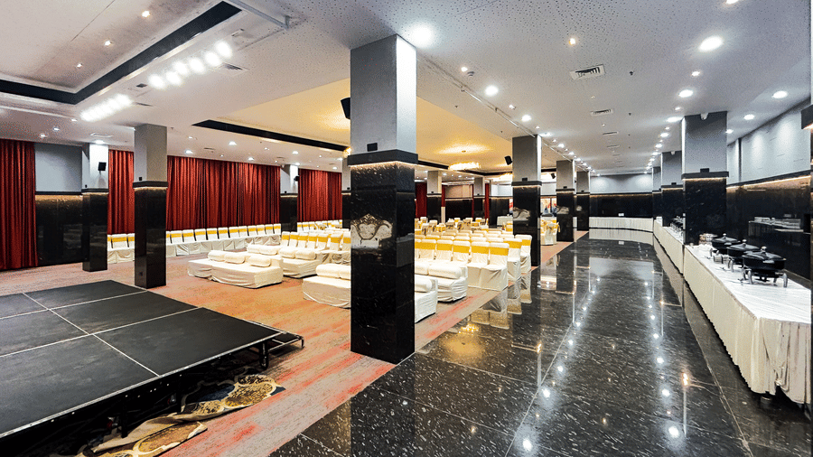 Spacious banquet hall with black marble floor, stage, and ceiling lights at Infiniti Hotel, Indore.