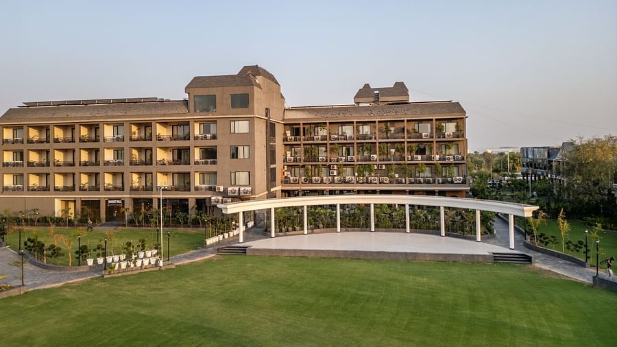 Hotel Highway King, Bagru, building with multiple balconies and a large green lawn in front under a clear sky. 