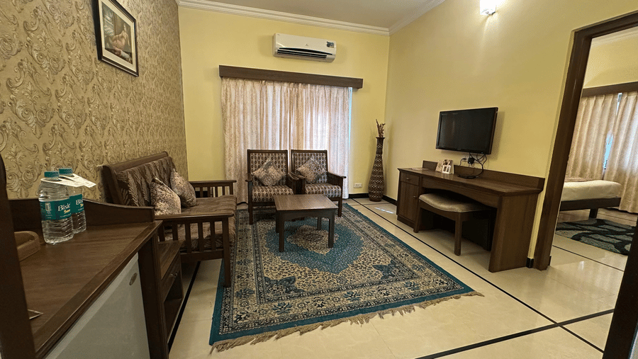 A living room at Amantra Shilpi Resort, Udaipur featuring 2 sofas, a television, a desk, and a patterned blue rug.