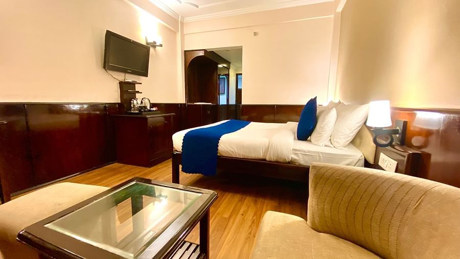 A view from a cushioned chair showcasing the bed and wall-mounted television at DLS Park Grace, Haridwar.