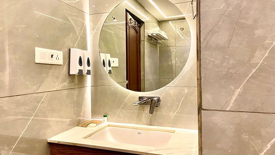 Interior view of a bathroom featuring a circular mirror above the wash basin at DLS Park Grace, Haridwar.