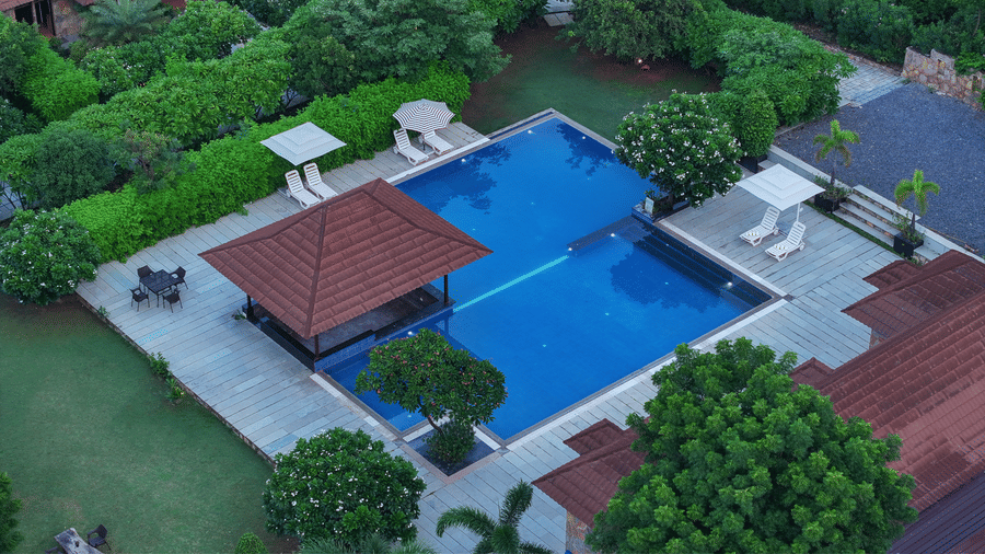 A high-angle view of a swimming pool with an adjacent pavilion and sun loungers | Anandam Jungle Retreat Resort, Udaipur