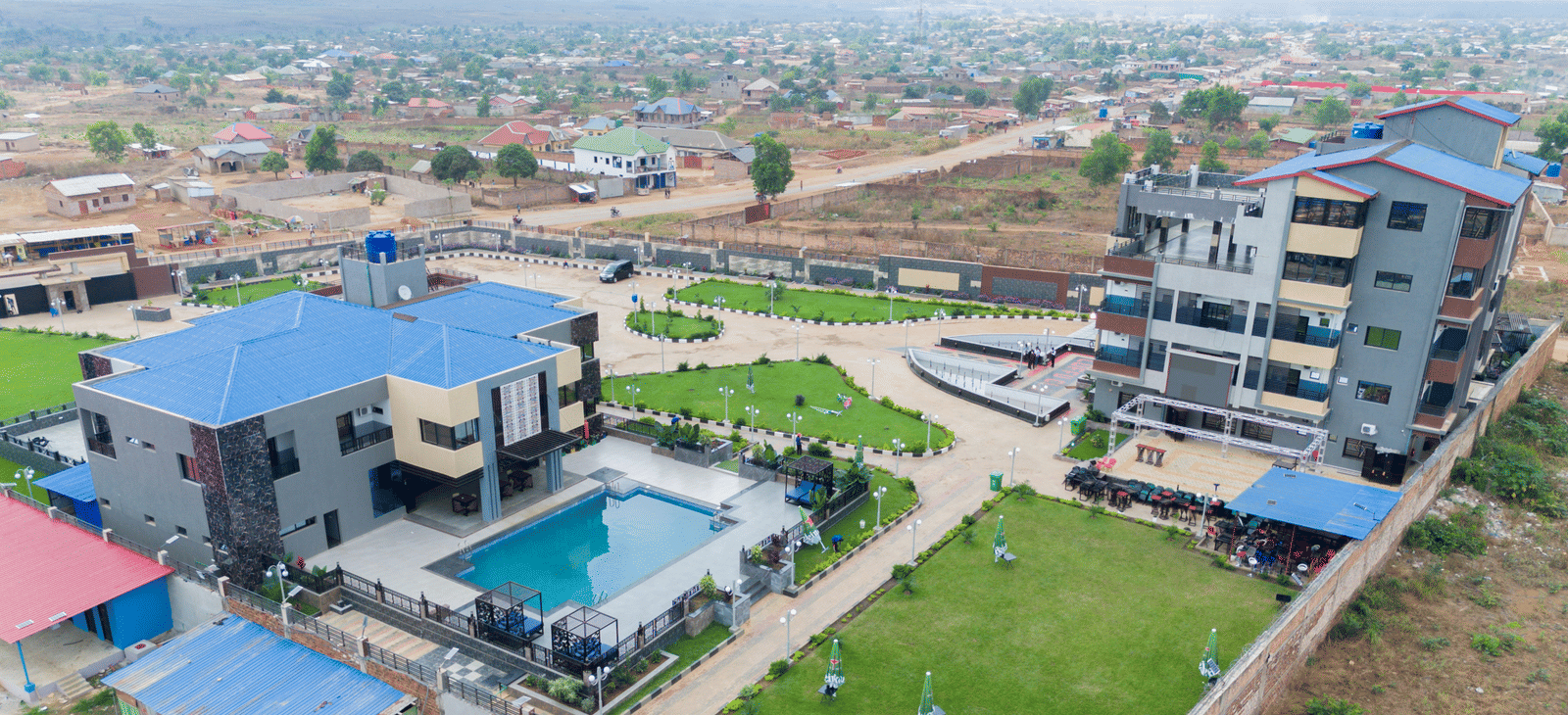 Wider aerial view of a building complex with a swimming pool, showing the surrounding neighbourhood - Luffu Club