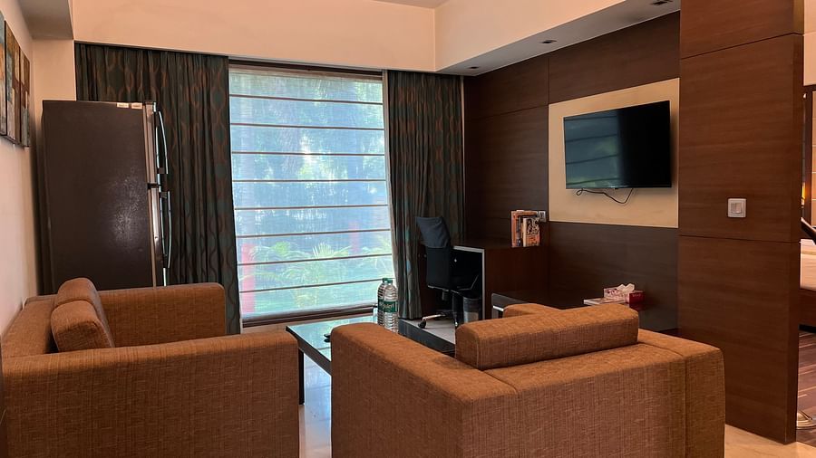 separate living room area with brown colour couches a television and curtained windows inside a suite room - yuhi mansions2