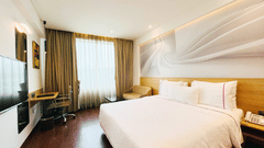  A corner view of deluxe room at Nemesia with a comfortable king-size bed, a work desk, a seating area, floor-to-ceiling windows with natural light, and a modern, artistic wall mural.