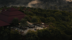 Aerial view of a forest resort surrounded by dense greenery and mist, with scattered seating areas.