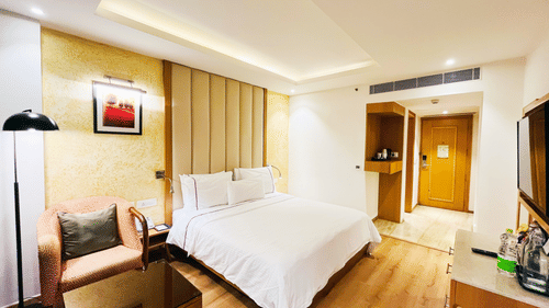 A side angle of the standard room at Nemesia featuring a king-size bed, a wall-hanging painting, a work desk, and a passage to the door.