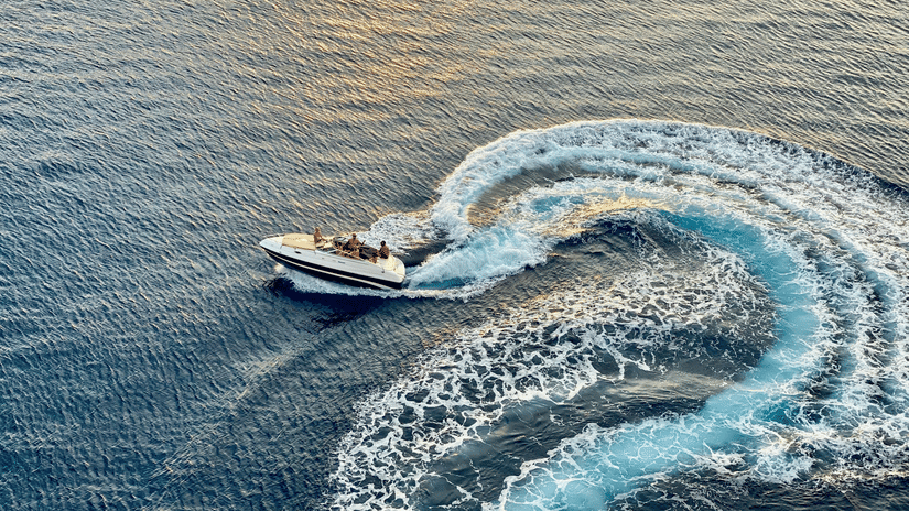 Aerial view of a white speedboat making a sharp turn on blue water leaving a wide foamy wake trail curving across the surface of the river.