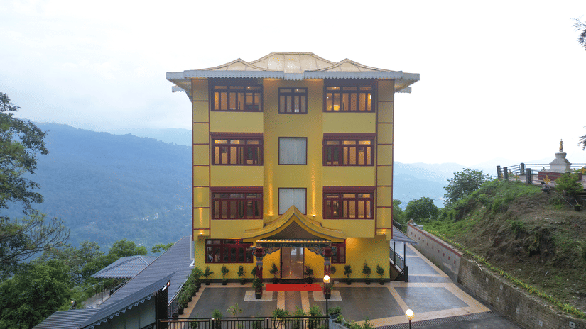 Exterior view of the Hotel Royal Retreat, a three-storey yellow building with a backdrop of  rolling hills.