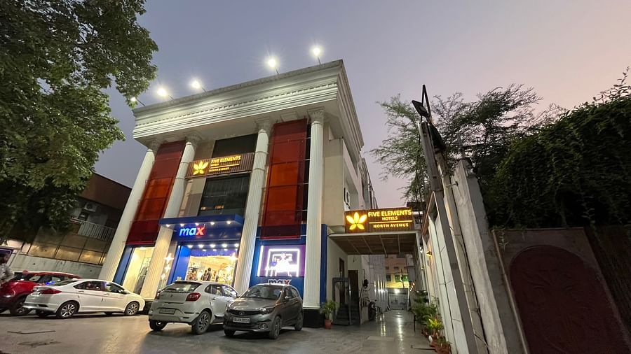 An image of a well lit facade of Five Elements Hotels North Avenue, Delhi which is surrounded by commercial buildings and trees