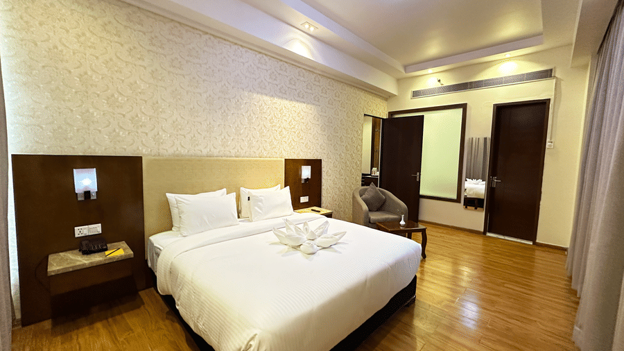 The Suite's king size bed at Golden Tulip Jaipur, Kukas, placed centrally, with bedside tables, over wooden flooring, and ample lighting.