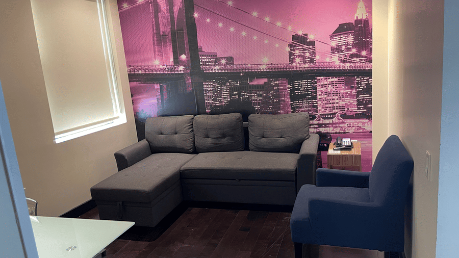 Contemporary lounge space at Night Hotel Broadway with an L-shaped sofa, armchair, and illuminated city scape wall art.