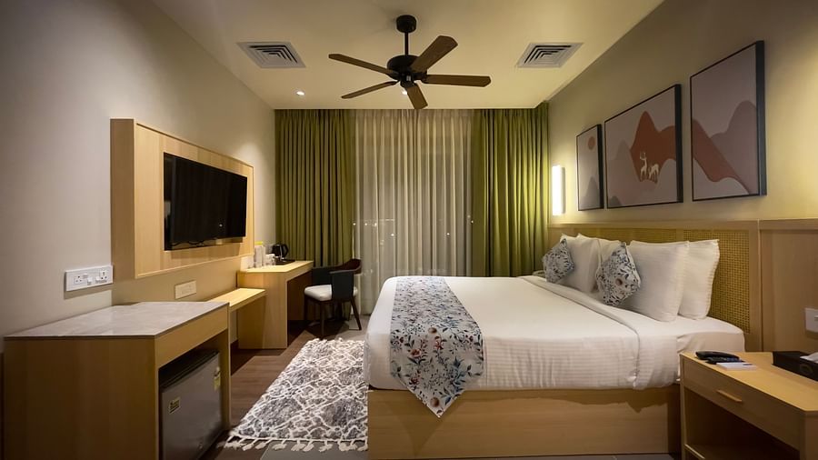 A double bed with fancy covers and cushions, with a flat screen television, work desk and wall hangings on the room.