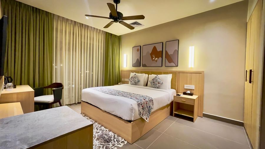 An image showing a double bed with fancy covers and cushions, with a flat screen television, work desk and wall hangings on the room.