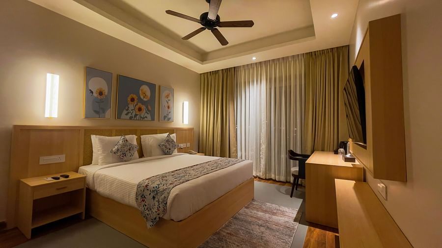 A double bed with cosy pillows, a work desk and chair, a TV, along with a ceiling fan and some wall paintings.