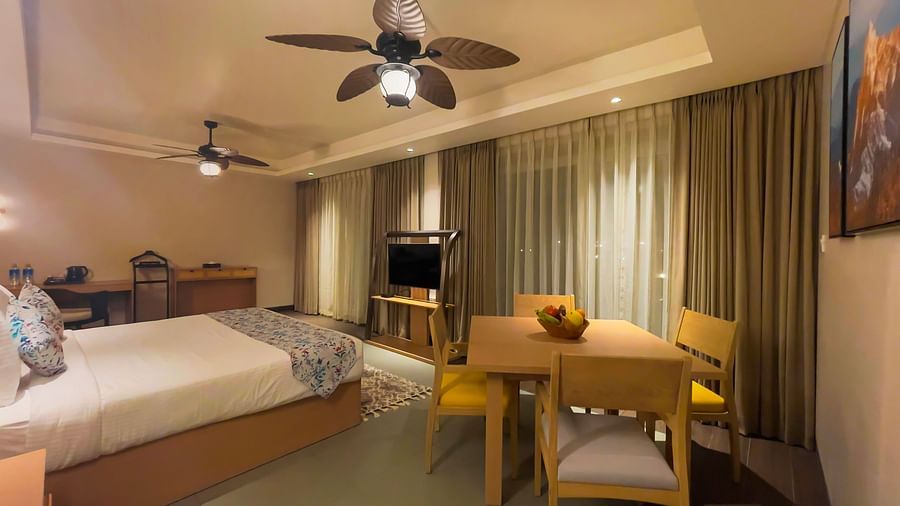 A large bed with pillows and coverlet, near a dining table for 4, with chairs, also a television and study area on the shot.