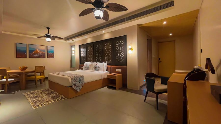 A double bed with dining area, a dedicated study area, with multiple chairs for seat up to 5 people, and two ceiling fans on the view.
