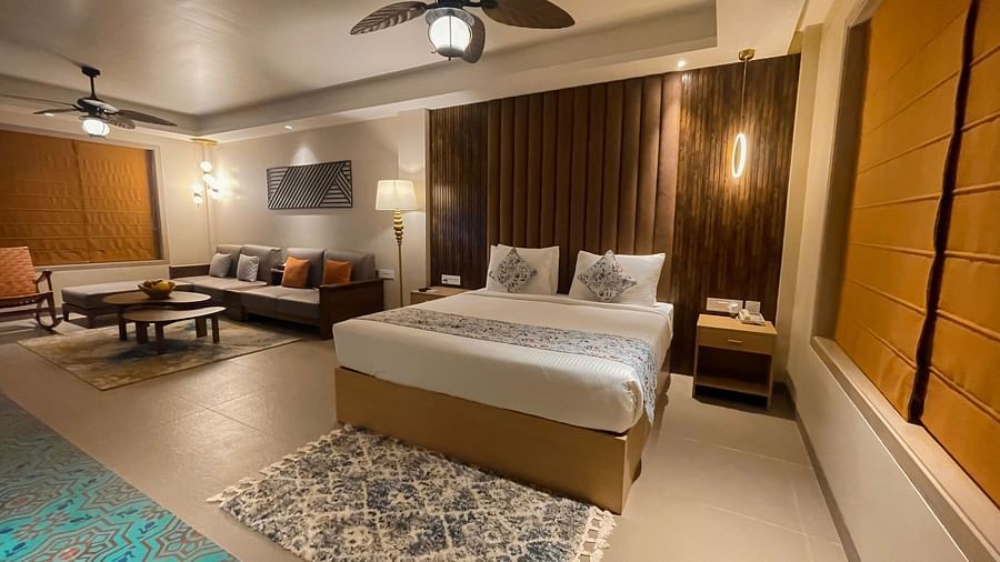 A double bed with pillows and cushions for two, near a living area with sofas, coffee table and a chair.