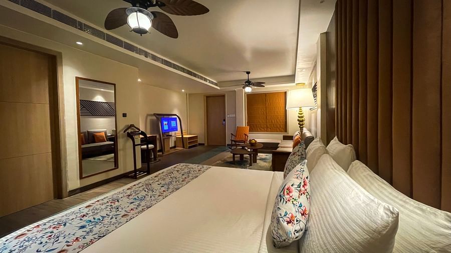 A suite with a large bedding with pillows and coverlets. Also, living area with sofas, coffee tables and a chair on the view.