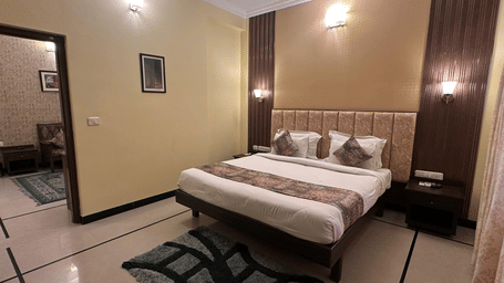A bedroom with a king size bed, a tall cushioned headboard, and wood-paneled walls in an interior view at Amantra Shilpi Resort, Udaipur.