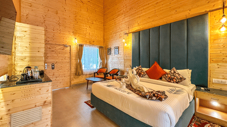 The spacious Sajjan Villa With Private Pool at Bamboo Saa Mulberry Resort, Pushkar, featuring a bed, seating area, bedside table and a curtained window.