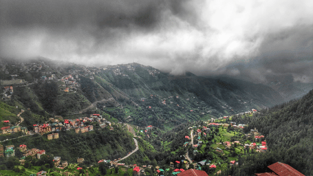 A small village with houses clustered on a hillside is shrouded in a misty, cloudy landscape.