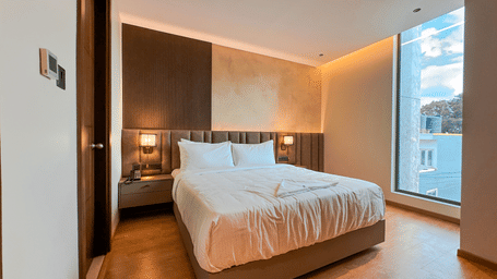 A wide-angle shot of the Executive Room featuring a plush double bed with bed side tables on either side of the bed at F Hotels, Bengaluru.
