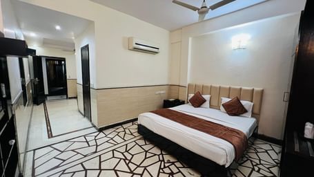 A well-appointed hotel suite featuring a comfortable bed with brown and white bedding, and a spacious layout. | Suite | Hotel Aadhar