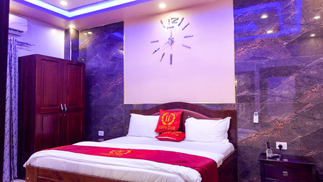 Hotel room interior with a bed, wall clock, wardrobe, and purple lighting - Luffu Club