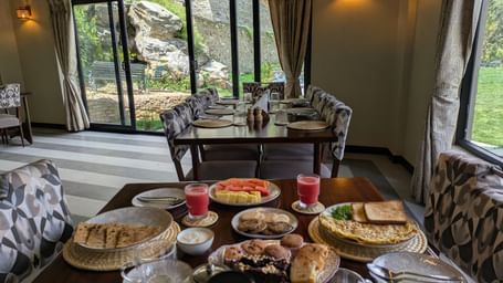 Dining space with large windows, serving breakfast with bread, fruit, and juice at The Chamomile Estate.
