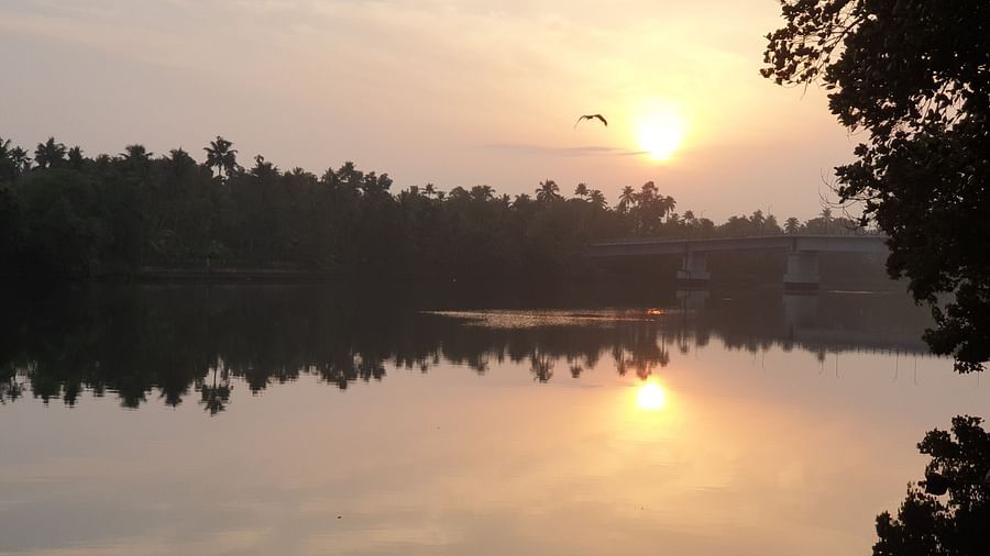 A tranquil landscape of a lake or river at sunset or sunrise, with reflections of the sky and trees on the water.