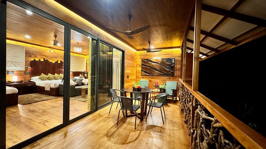 A tree house with large glass windows and a wooden balcony overlooking the surroundings at night - BluSalzz Collection - Tranquil Resort, Wayanad